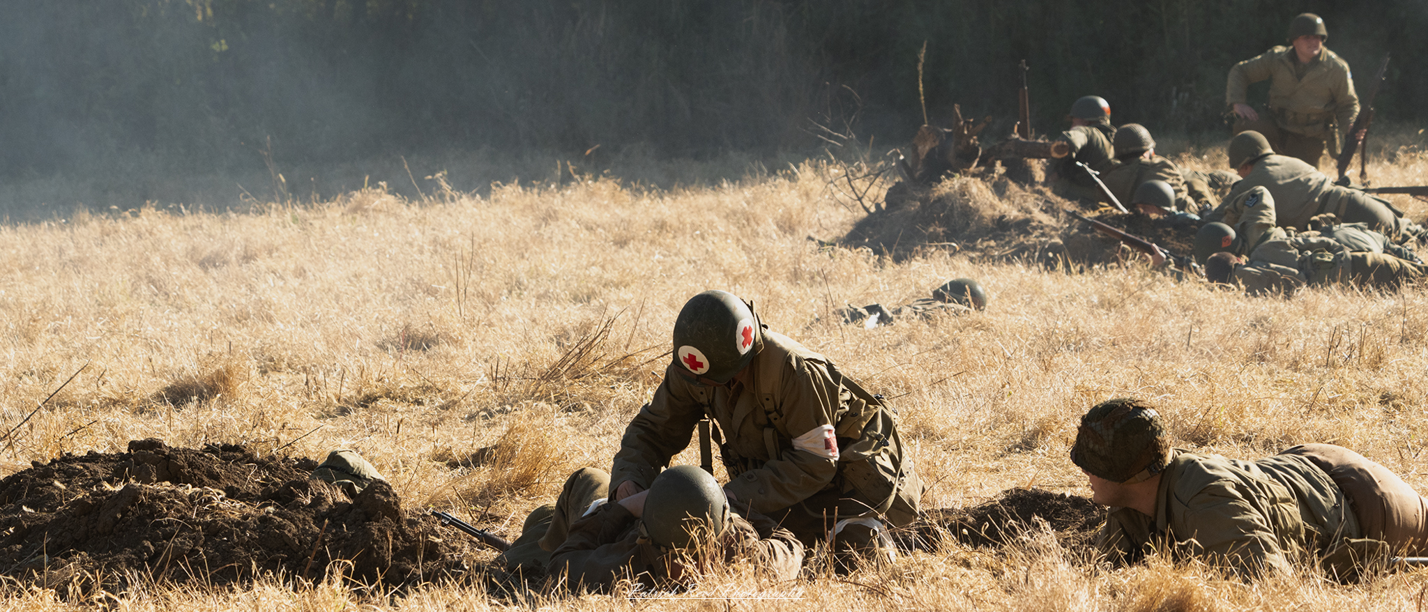 "Image of a World War II medic in the field, wearing a standard military uniform with a red cross armband. The medic is kneeling beside a wounded soldier, providing first aid in a grassy area that shows signs of battle. The medic's focused expression conveys determination and compassion as they attend to the injured comrade. In the background, there are hints of military equipment and other soldiers, emphasizing the urgency of the situation. The overall scene captures the bravery and dedication of medics during wartime."